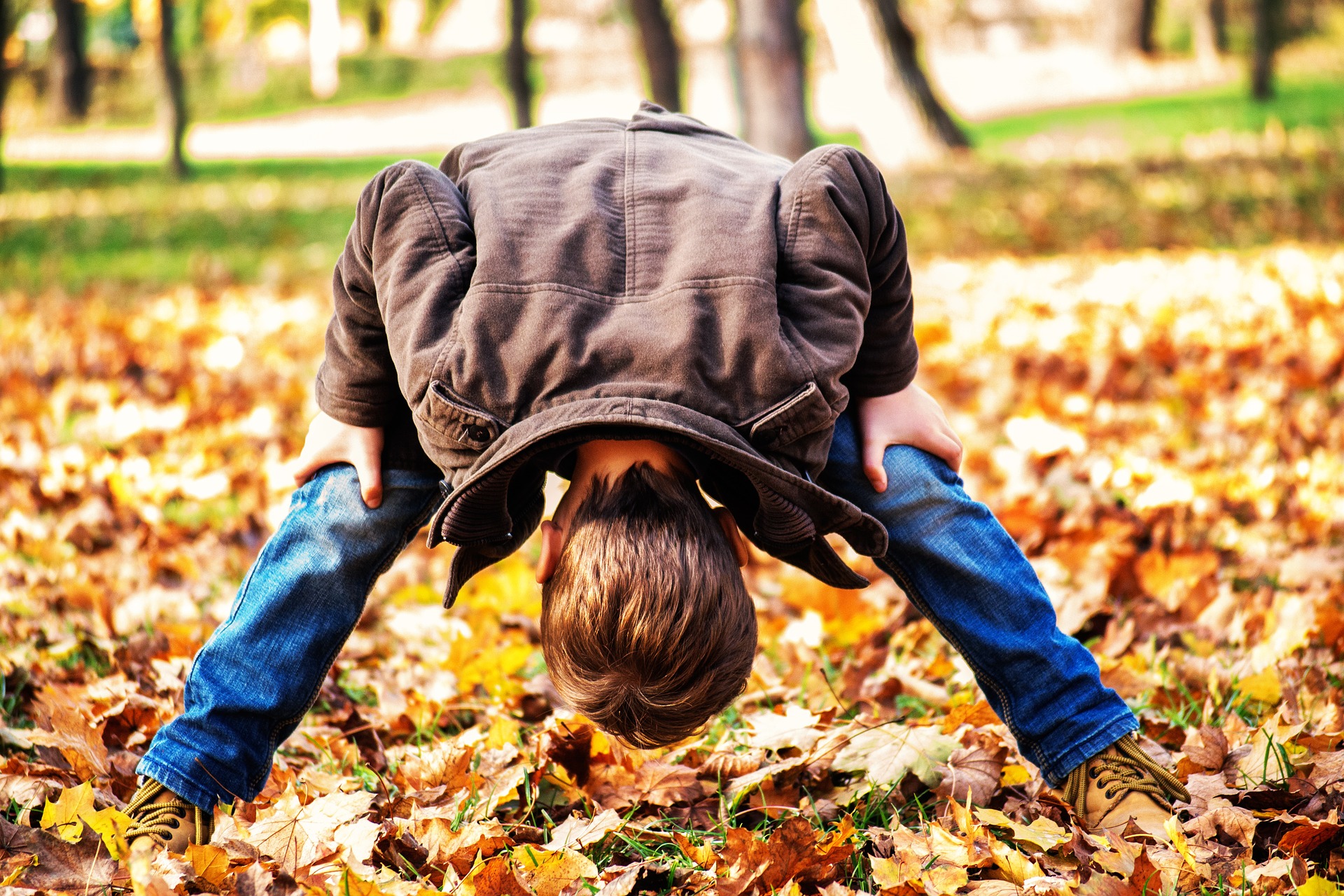 Junge steht im bunten Herbstlaub und schaut kopfüber zwischen seinen Beinen hindurch