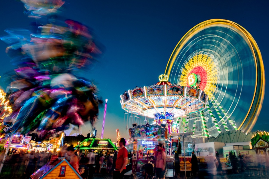 Beleuchtete Kirmes in der Abenddämmerung mit Riesenrad und Kettenkarussell