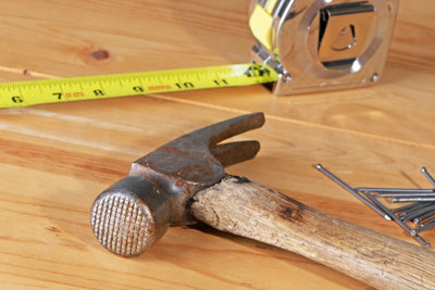 Hammer, Maßband und Nägel liegen auf einer Holzplatte bereit