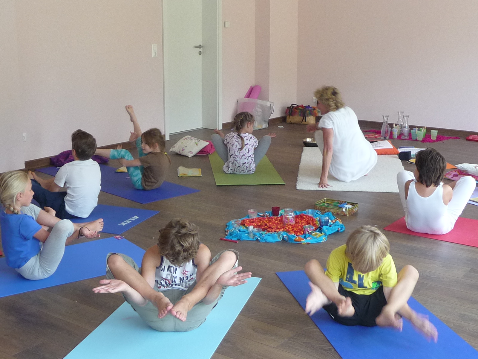 Kindergruppe sitzt auf bunten Yogamatten und macht mit einer Trainerin eine Balanceübung